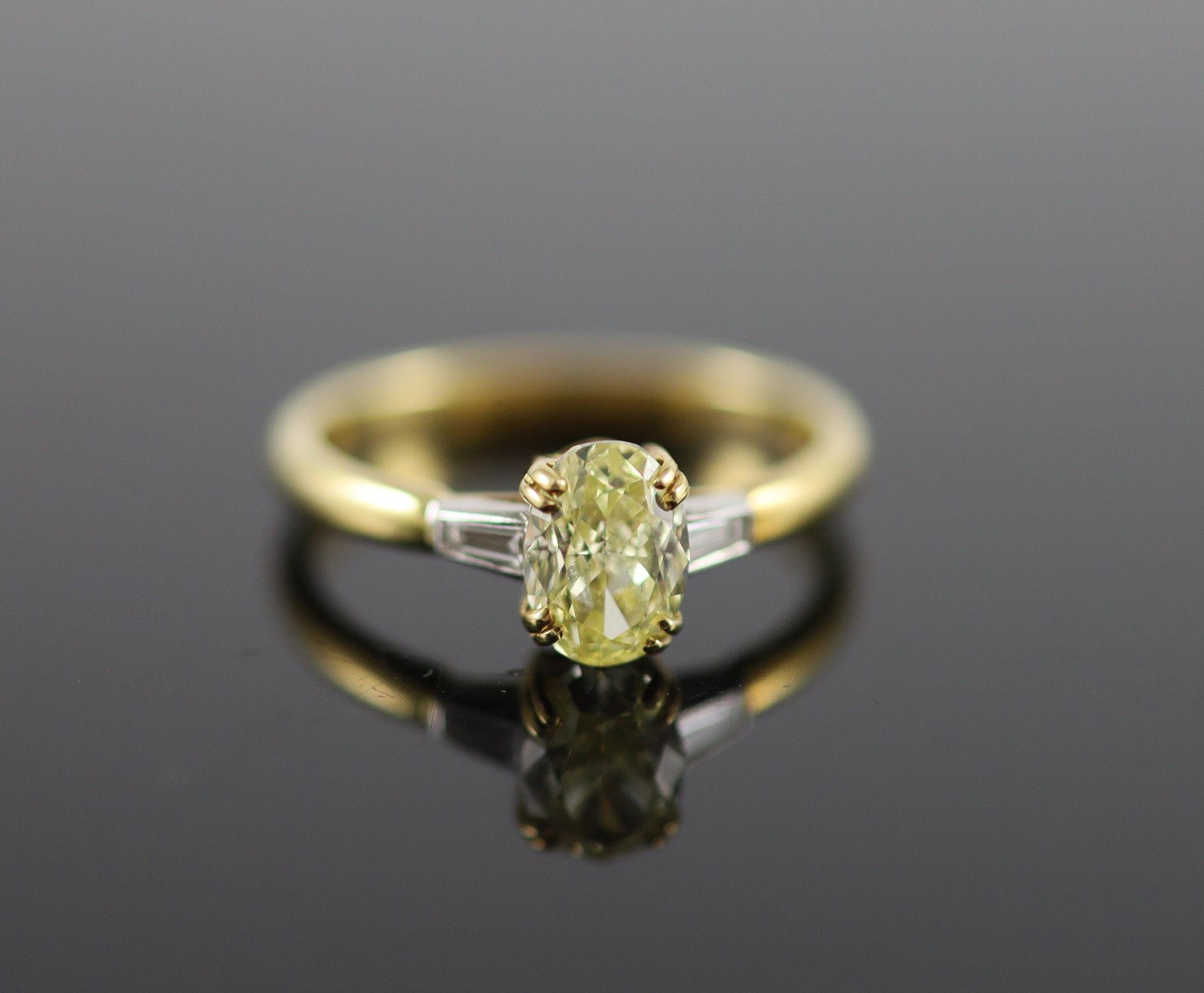 A modern 18ct gold and single stone oval fancy yellow diamond ring, with trapeze cut diamond set shoulders